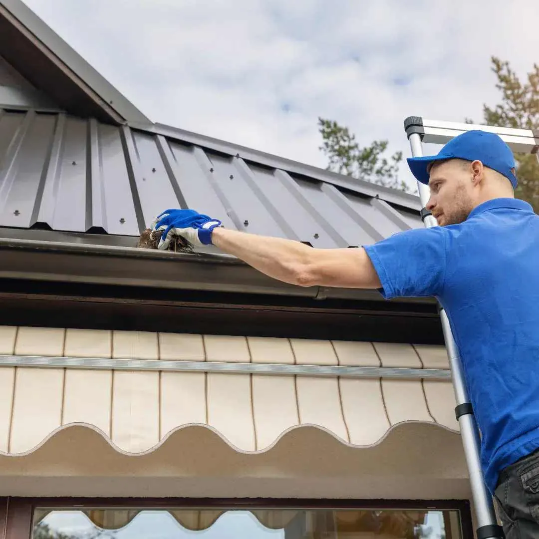 Technician working on a gutter at the roof edge from a ladder